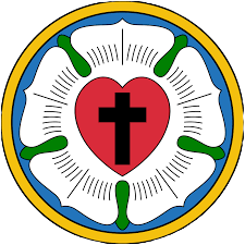 Image of Luther's Rose, a symbol of the Lutheran Church. The emblem features a black cross in the center of a red heart, symbolizing faith in Jesus Christ and the love and life that come from faith. The heart is set inside a white rose, representing the joy, comfort, and peace of faith. The rose is surrounded by a blue field, signifying the heavenly joy and hope of eternal life, and encircled by a gold ring, symbolizing the eternal and priceless nature of God's grace. We are an LCMS church located in Fairhope, AL.